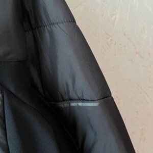 May include: Close-up of a black jacket with a quilted design. The jacket has a smooth, shiny texture and a reflective strip detail. The garment appears to be made of a lightweight material.