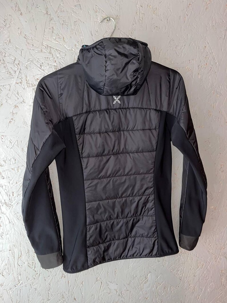 May include: Black hooded jacket with a quilted back panel and side panels. The jacket has long sleeves and a small white logo on the upper back. The jacket is hanging on a metal hanger.