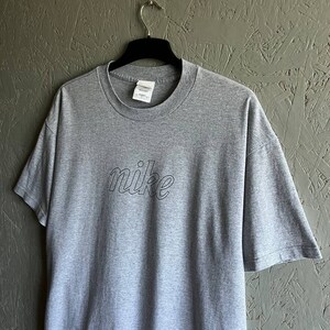 May include: Grey t-shirt with a black outline of the word "nike" on the front.