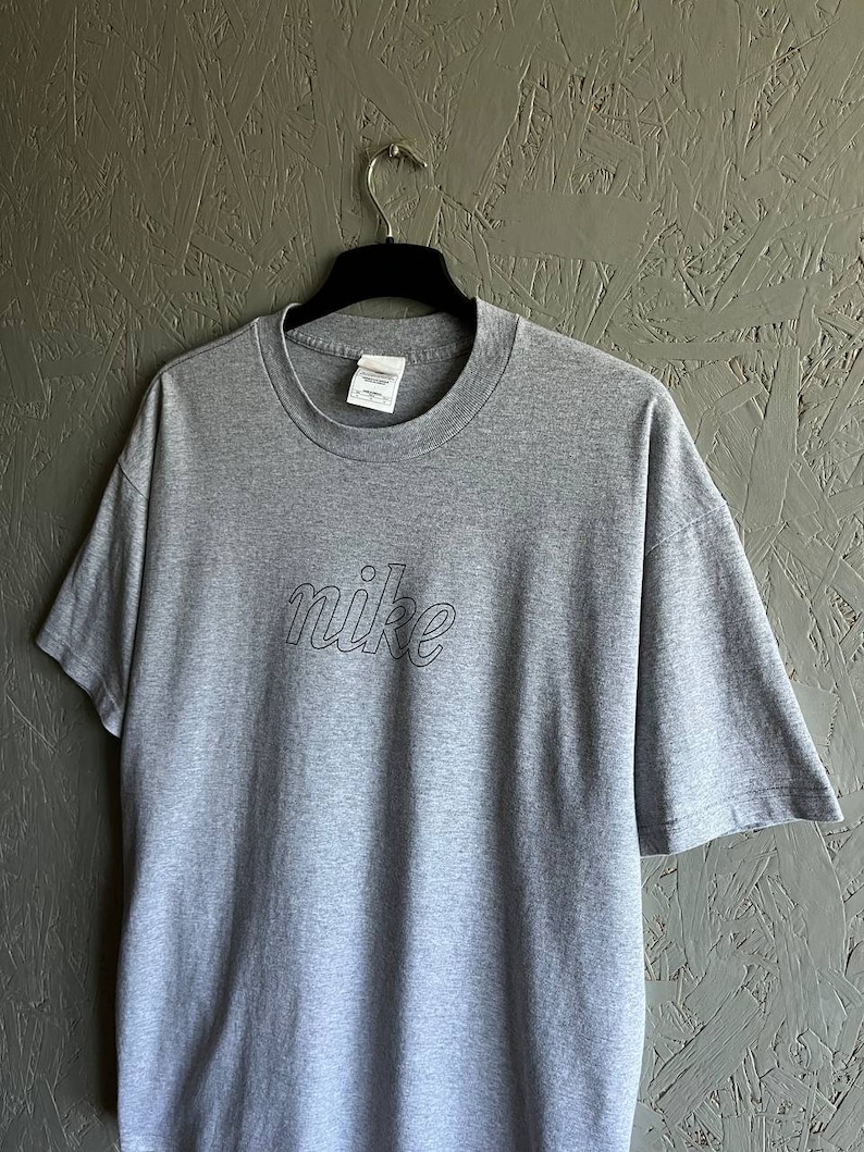 May include: Grey t-shirt with a black outline of the word "nike" on the front.