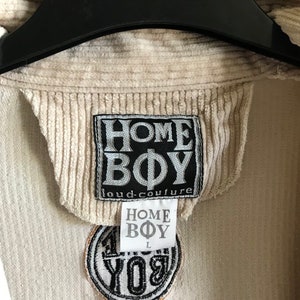 May include: A beige corduroy jacket with a black "HOME BOY loud-couture" label and a black and white embroidered patch that says "HOME BOY" in a circle.