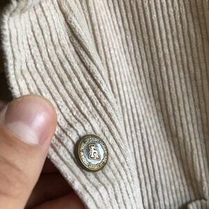 May include: A close-up of a beige corduroy fabric with a gold button that reads "The Legacy Way, Homebody, Chicago, Paris".
