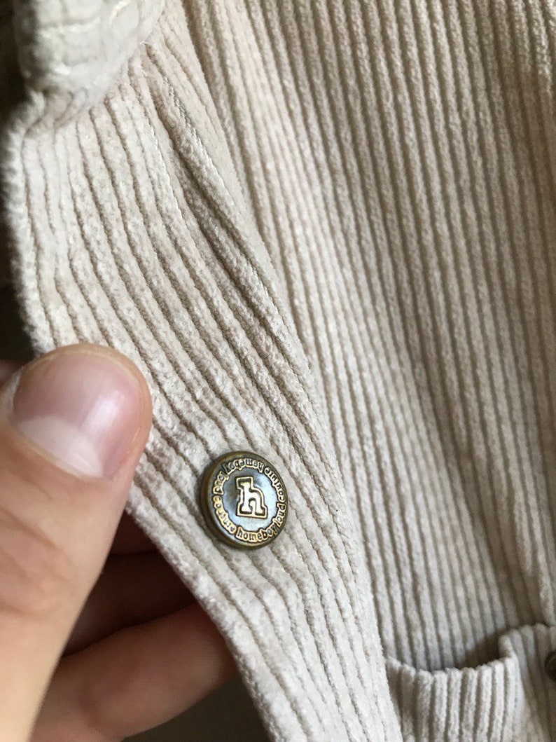 May include: A close-up of a beige corduroy fabric with a gold button that reads "The Legacy Way, Homebody, Chicago, Paris".