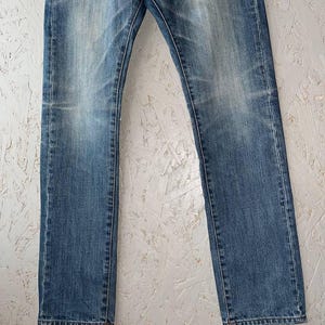 以下が含まれることがあります： 色あせたブルーデニムのジーンズ。クラシックなストレートレッグフィット。ジーンズは、微妙な摩耗パターンと色あせを示し、伝統的な5ポケットデザインとボタンとジッパーの留め具を備えています。デニムは中程度の重さで、わずかに着用された外観をしています。