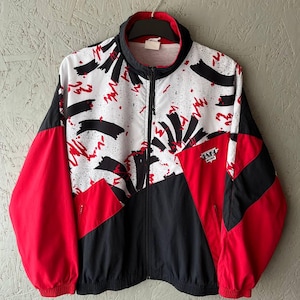 May include: A vintage zip-up jacket with a striking color-block design. The jacket features red sleeves, black panels, and a white upper section adorned with black brushstroke and red splatter patterns. The collar and cuffs are black and red.