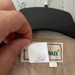 May include: A tan garment featuring a rectangular label with the text L.L.Bean in green lettering. A white care instruction tag is attached, displaying text in both English and French, including instructions for machine washing and low temperature ironing.