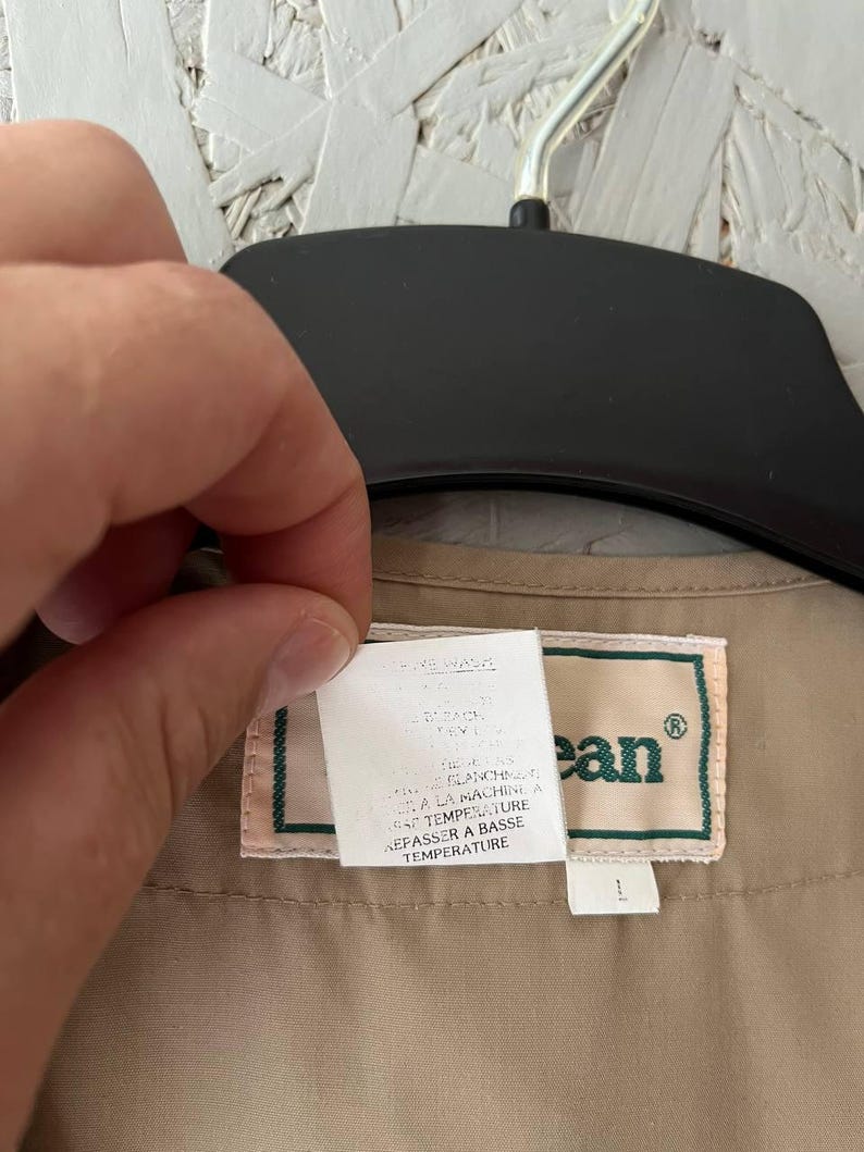 May include: A tan garment featuring a rectangular label with the text L.L.Bean in green lettering. A white care instruction tag is attached, displaying text in both English and French, including instructions for machine washing and low temperature ironing.