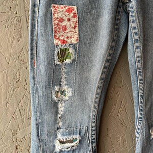 Puede incluir: Vaqueros de mezclilla azul claro con parches decorativos. Los parches son de tela floral en rojo y blanco, y patrones verdes y azules. Los vaqueros tienen detalles desgastados con costuras visibles.