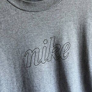 May include: A heather grey t-shirt with a black outline of the word "nike" in a stylised font.