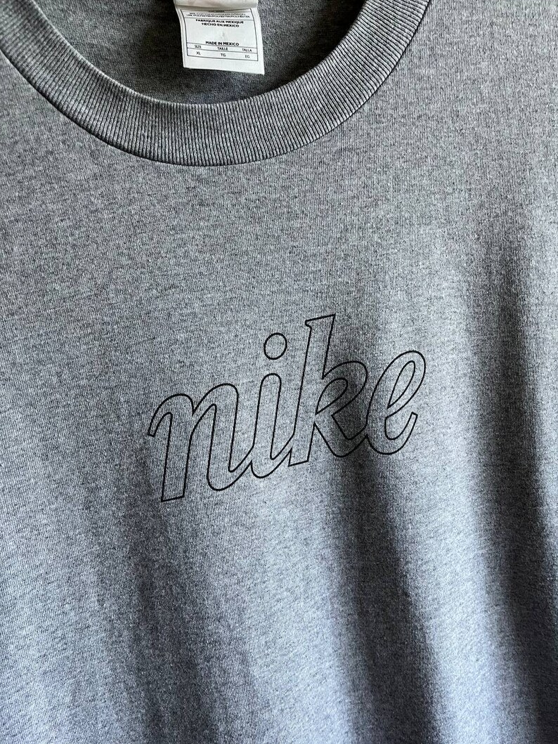 May include: A heather grey t-shirt with a black outline of the word "nike" in a stylised font.