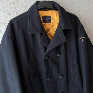 May include: A dark blue peacoat with a double breasted closure and a gold and black logo that says "Paul & Shark" and "Bretagne".
