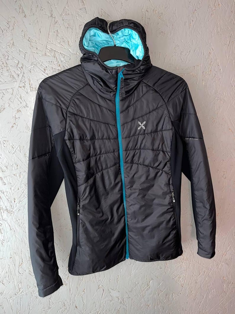 May include: Black hooded jacket with a light blue interior and a turquoise zip. The jacket has a quilted design on the front and a small white logo on the chest. The sleeves are black and the jacket is hanging on a black hanger.