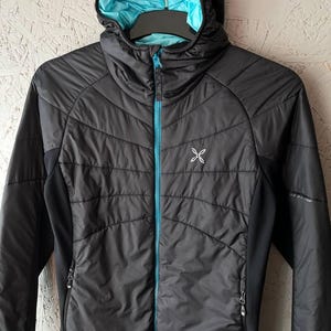 May include: A black hooded jacket with a turquoise zip and lining. The jacket features a quilted design on the front and a small white logo on the chest. The jacket is hanging on a black hanger.