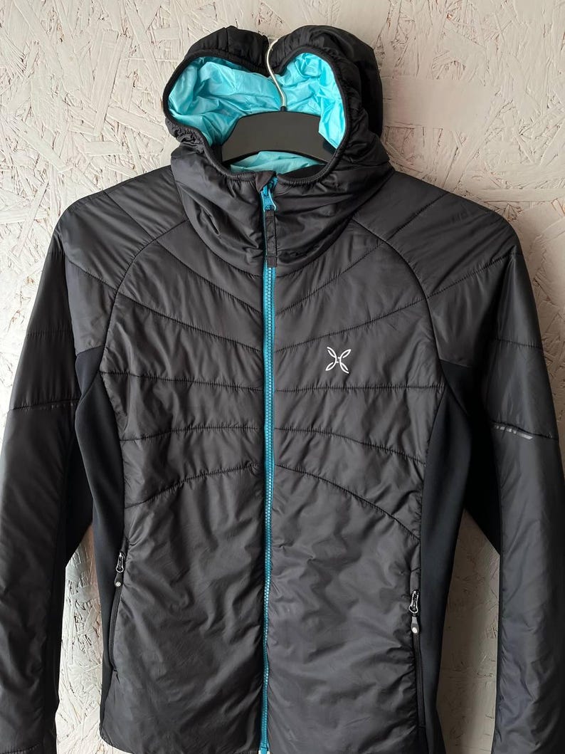 May include: A black hooded jacket with a turquoise zip and lining. The jacket features a quilted design on the front and a small white logo on the chest. The jacket is hanging on a black hanger.