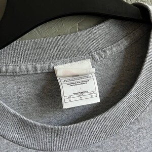 May include: Grey t-shirt with a white tag that reads "92% Cotton/Algodon 8% Polyester/Polyester/Polyester Fabrique aux Mexique Hecho en Mexico" and "Made in Mexico" with size information: XL, TG, EG.