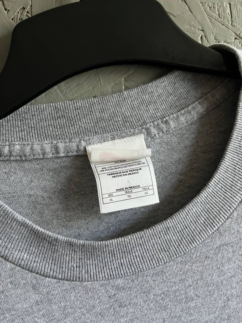 May include: Grey t-shirt with a white tag that reads "92% Cotton/Algodon 8% Polyester/Polyester/Polyester Fabrique aux Mexique Hecho en Mexico" and "Made in Mexico" with size information: XL, TG, EG.