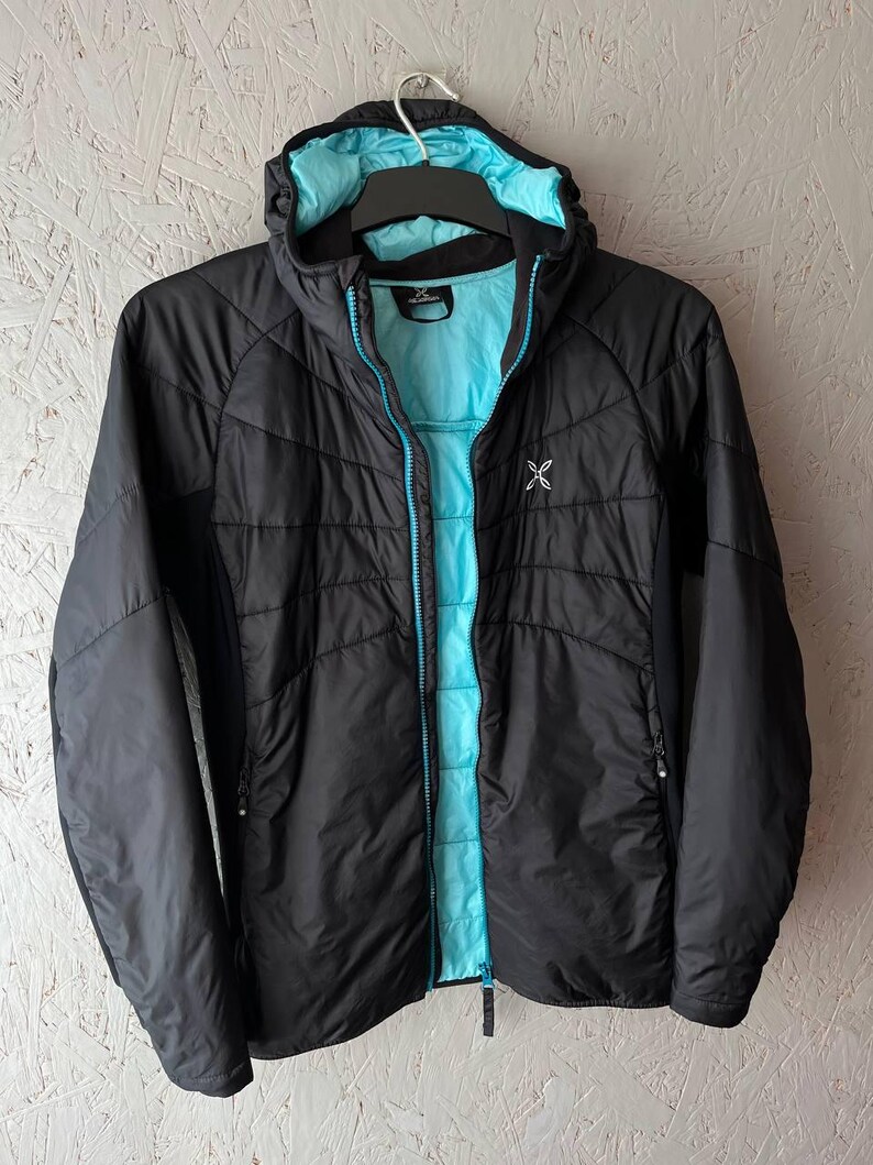 May include: Black hooded jacket with a turquoise interior and zip. The jacket has a quilted design and a small white logo on the chest. The hood and zip are outlined in turquoise. The jacket is hanging on a black hanger.