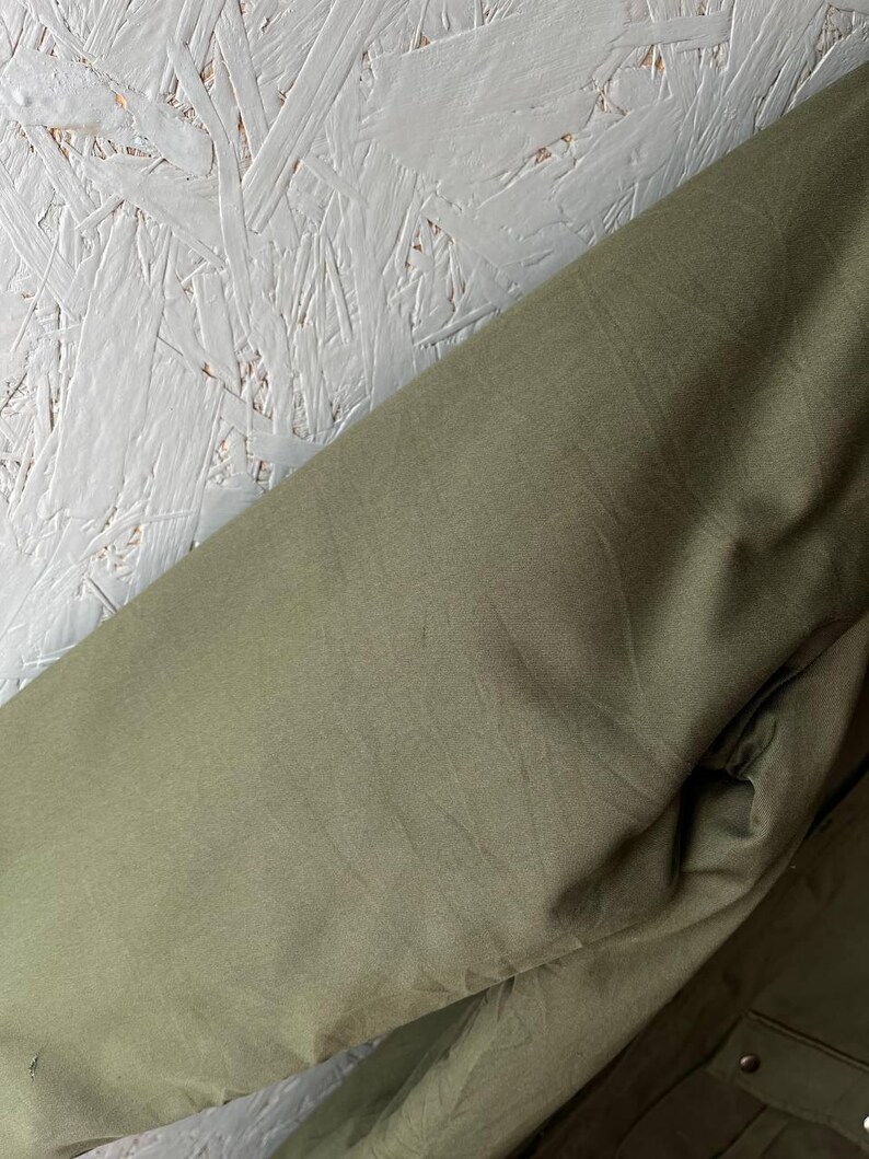 K&ouml;nnte beinhalten: Ein olivgr&uuml;ner Jacken&auml;rmel aus einem glatten, einfarbigen Stoff. Der &Auml;rmel hat einen geraden Schnitt und ein schlichtes Design ohne sichtbare Muster, Texturen oder zus&auml;tzliche Beschl&auml;ge auf dem sichtbaren Teil des Kleidungsst&uuml;cks.