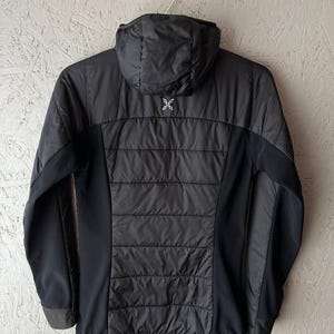 May include: Black hooded jacket with a quilted central panel and solid black side panels. The jacket has a zip closure and a small white logo on the upper back. The jacket is hanging on a silver hanger.