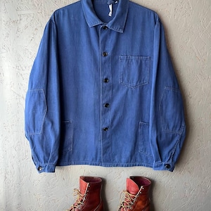 May include: A blue long-sleeve button-up jacket with a collar, a single chest pocket, and two lower pockets, paired with a pair of brown leather lace-up boots featuring yellow and red laces and thick black rubber soles.