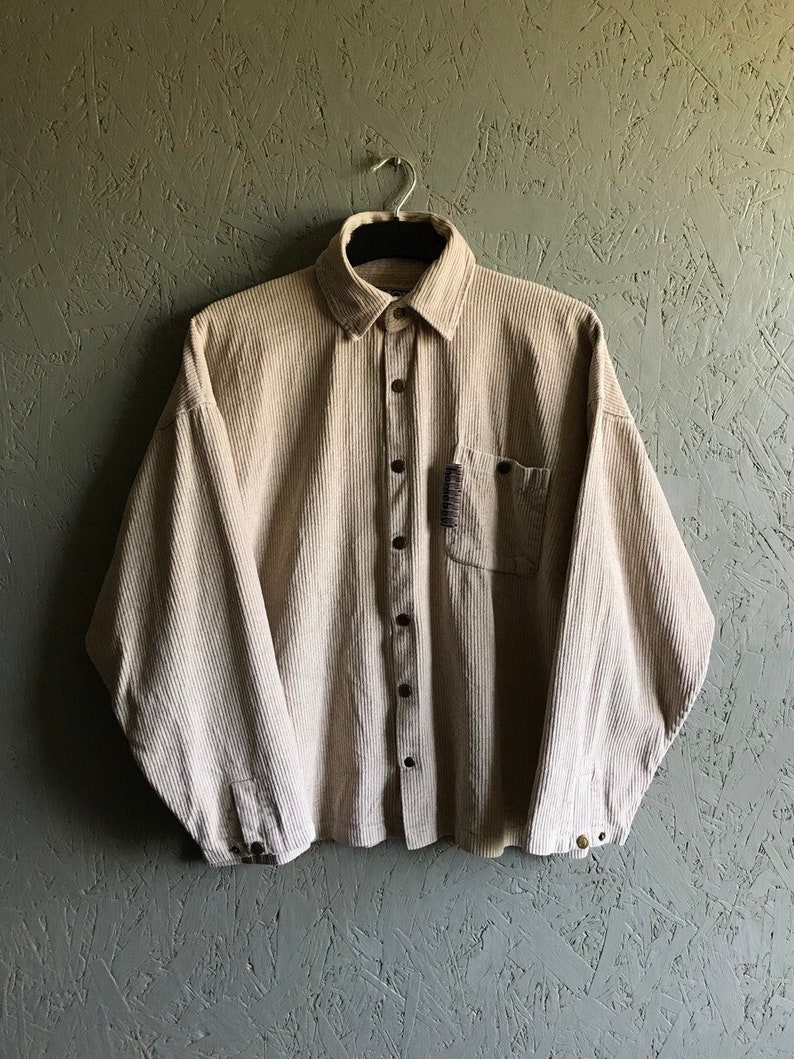 May include: A beige corduroy button-up shirt with long sleeves and a single chest pocket.