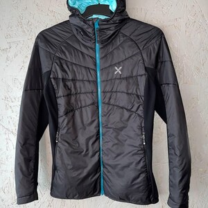 May include: Black hooded jacket with a light blue lining and a matching blue zip. The jacket features a quilted design on the front and a small white logo on the chest. The sleeves and side panels are solid black.