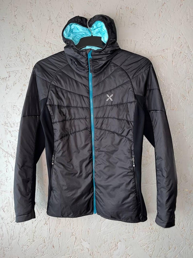 May include: Black hooded jacket with a light blue lining and a matching blue zip. The jacket features a quilted design on the front and a small white logo on the chest. The sleeves and side panels are solid black.