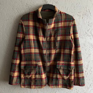Peut inclure: Une veste en plaid marron, rouge et jaune avec une fermeture éclair et deux grandes poches. La veste a un col et des manches longues.