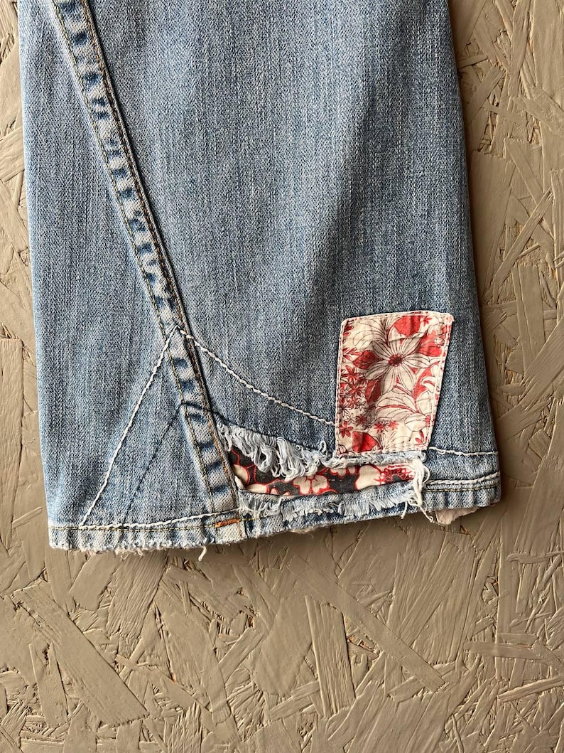 Puede incluir: Vaqueros de mezclilla azul claro con un parche floral. Los vaqueros presentan un dise&ntilde;o de costura &uacute;nico y un dobladillo deshilachado. El parche es rojo y blanco con un estampado floral. Los vaqueros est&aacute;n hechos de mezclilla duradera.