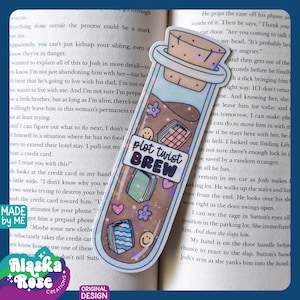 May include: A clear, corked vial sticker with the text "plot twist BREW" and various small illustrations. The sticker has a holographic effect and is placed on a book page.