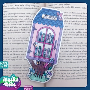 May include: A whimsical sticker featuring a tiny library design. The sticker showcases a pink and blue building with a window displaying colorful books. Bees and flowers add to the charming aesthetic. Text on the sticker reads "Tiny Library: Take a Book, Leave a Book."