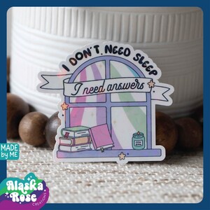 May include: A sticker with a window design and the text "I don't need sleep I need answers". The window has a stack of books and a candle inside. The sticker is on a light brown surface.
