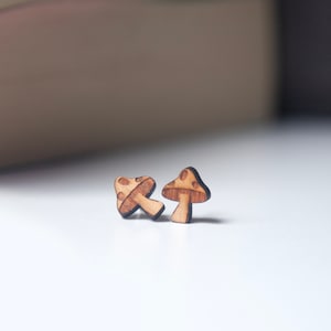 May include: A pair of wooden mushroom earrings. The earrings are brown with a light brown stem and a dark brown cap with white spots.