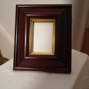 May include: A dark brown wooden picture frame with a gold inner border. The frame is empty.