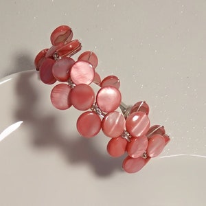 May include: A pink and white shell bracelet on a white heart-shaped plate.