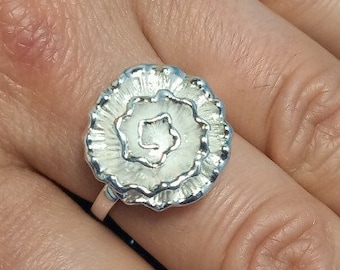 May include: A silver ring with a flower-shaped design. The ring is on a finger with a light pink nail polish.