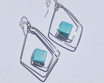 Può includere: Un paio di orecchini d'argento con accenti di pietra turchese. Gli orecchini presentano un design geometrico con più strati di filo.