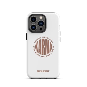 Könnte beinhalten: Weißes Handycase mit einem braunen, kreisförmigen Design, das in der Mitte "KARMA" trägt, umgeben von dem Text "ENERGY CIRCULATES EVEN WHEN YOU DON'T SEE IT". Der Markenname "OOPSI STUDIO" ist unten aufgedruckt.