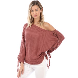 May include: A mauve knitted sweater with a loose fit and long sleeves. The sweater has a lace-up detail on the sleeves and a slightly off-the-shoulder neckline.