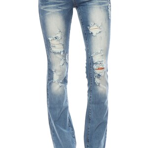 May include: Light blue denim jeans with distressed details, featuring ripped sections on the front of the legs. The jeans have a classic five-pocket design and a straight leg fit. The model is wearing black sandals.