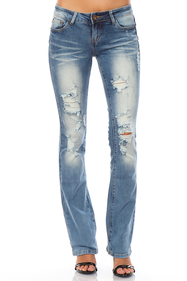 May include: Light blue denim jeans with distressed details, featuring ripped sections on the front of the legs. The jeans have a classic five-pocket design and a straight leg fit. The model is wearing black sandals.