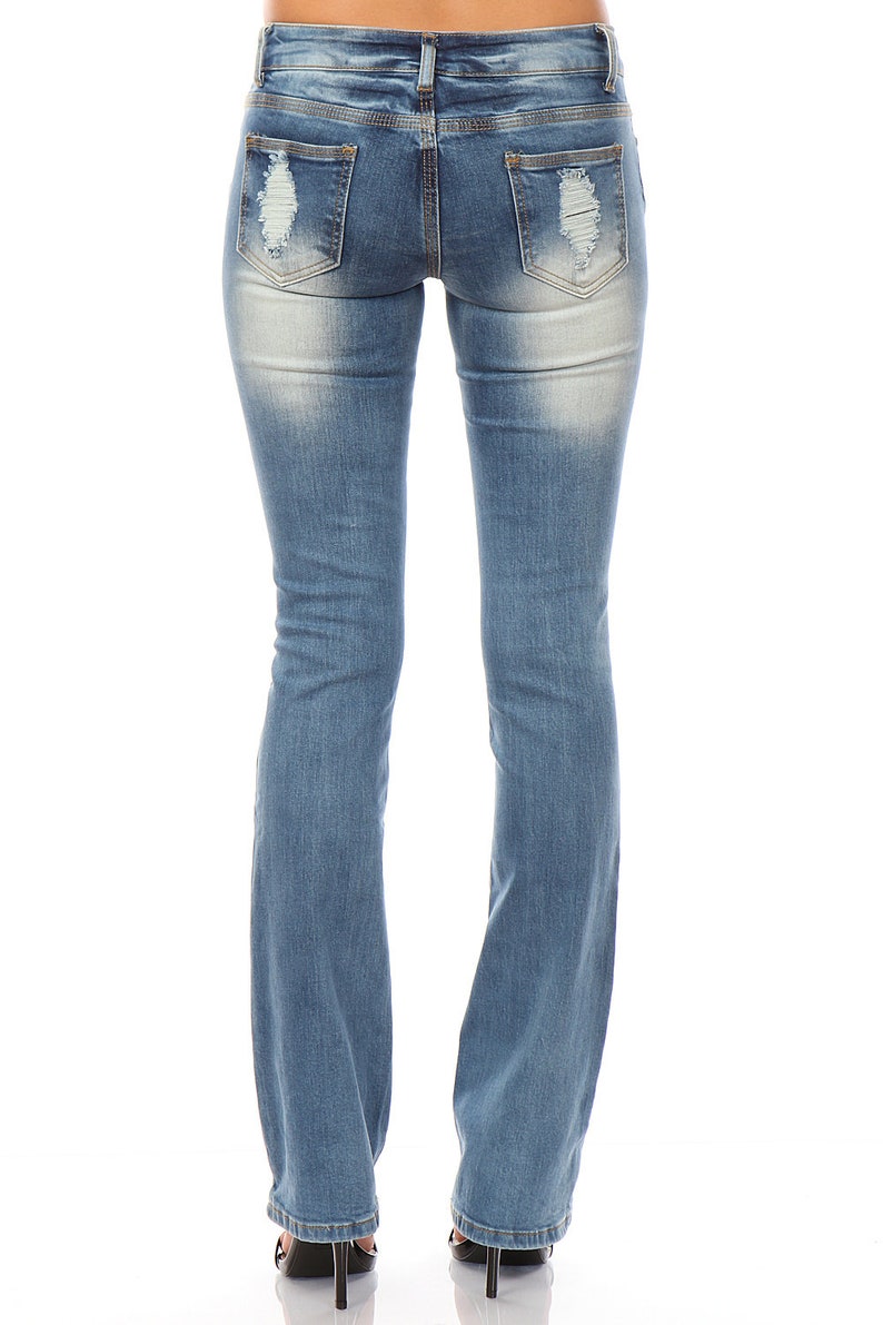 May include: Light blue denim jeans with distressed details on the back pockets. The jeans have a bootcut leg opening and are worn with black high heels. The jeans are faded in areas for a worn look.