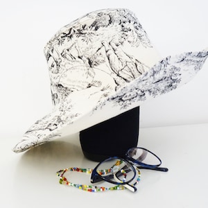 Grand chapeau à larges bords en Toile de Jouy blanche, fait main en France. Élégant et intemporel, il protège du soleil avec style. Doublure unie et surpiqûres raffinées sur la capeline pour une finition haut de gamme. Accessoire chic pour mariage, cérémonie, jardin ou plage. Idée cadeau femme, accessoire mode français, parfait pour la fête des mères, un anniversaire ou une escapade élégante sous le soleil