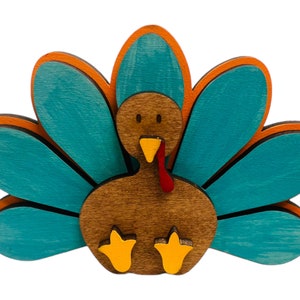 May include: A wooden turkey figurine with a brown body, red wattle, and yellow feet. The turkey has a teal blue tail with orange accents.