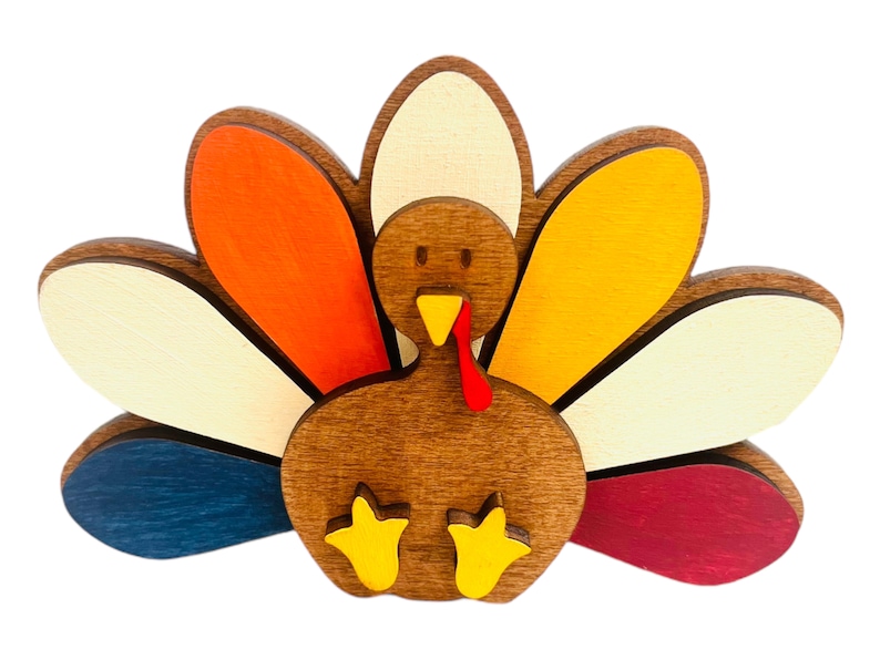 May include: A wooden turkey figurine with a brown body and a colorful tail. The tail feathers are painted in shades of orange, yellow, white, blue, and red.