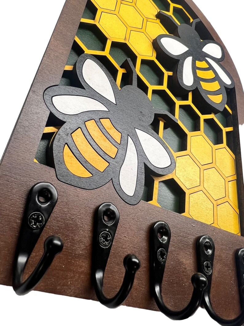 May include: Wooden key holder with a honeycomb design and two bees. The holder has five black metal hooks.