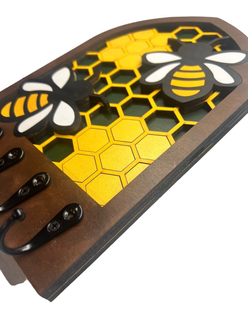 May include: Wooden key holder with a honeycomb design and two bees. The key holder has three hooks for hanging keys.