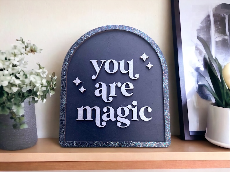 Pu&ograve; includere: Un cartello ad arco di colore blu scuro e scintillante con il testo "you are magic" in lettere bianche.