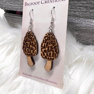 May include: A pair of wooden earrings shaped like morel mushrooms with silver hooks. The earrings are handmade in Northern Minnesota. Bigfoot Creations.