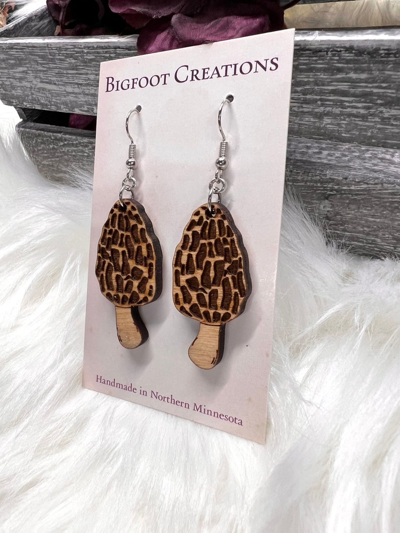 May include: A pair of wooden earrings shaped like morel mushrooms with silver hooks. The earrings are handmade in Northern Minnesota. Bigfoot Creations.